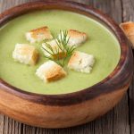 Organic green cream soup vegetarian lunch in bowl on vintage wooden background